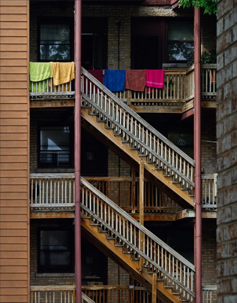 Colorful beach towels hanging from the railing of a third floor apartment.