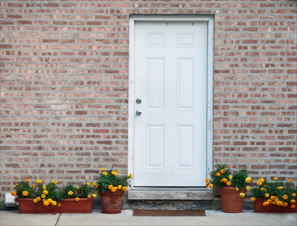 Marigolds in pots near a plain white door in a blank brick wall.