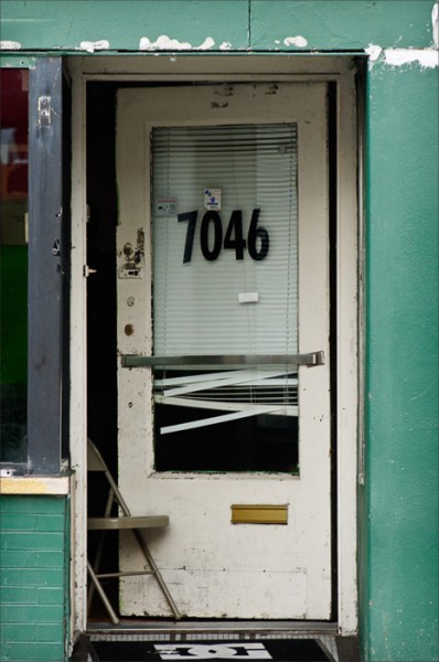 On a hot summer day, a metal folding chair holds a battered door partially open to the street.