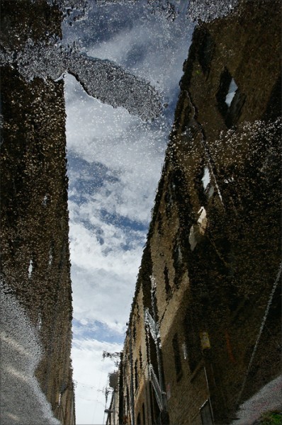 Alley buildings and sky reflected in water. 