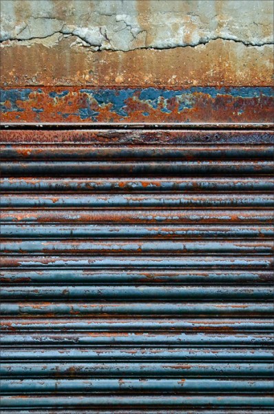 Horizontal lines of a colorful rusted door and concrete.