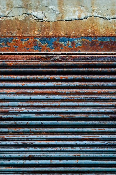 Horizontal lines of a colorful rusted door and concrete.