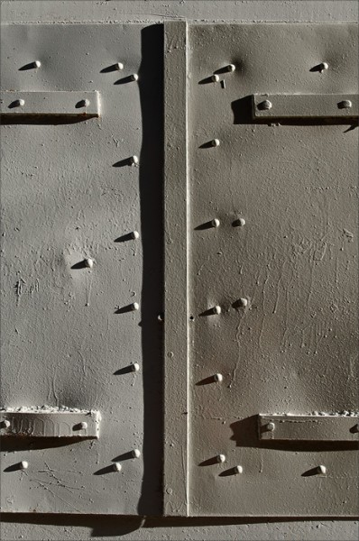 In morning sidelight, shadows play off the rivets of a metal door.