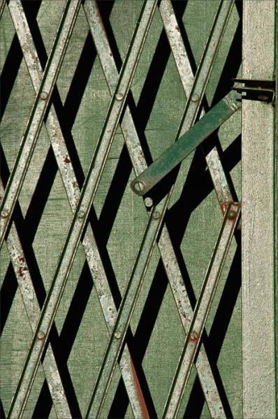 In morning sidelight, shadows play off the lattice bars of a metal gate.